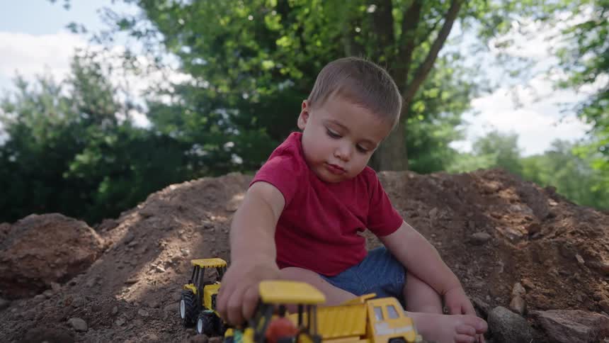 A toddler plays with toy construction trucks in a dirt pile