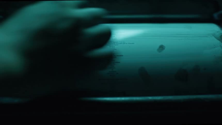 In a dimly lit facility a hand repeatedly wipes clean a large cylindrical roller on an industrial printing press