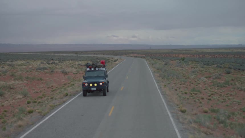 Flat barren land with jeep driving with stuff tied to roof