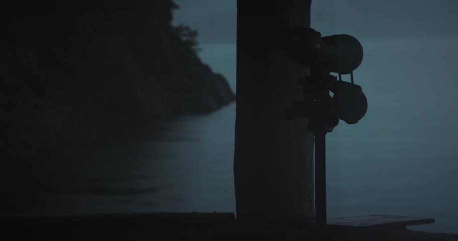 Telescope on tripod is positioned on dark balcony overlooking lake at dusk