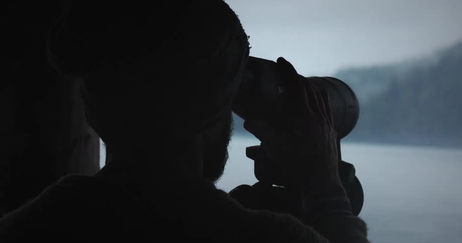 A man is looking at the shore with a binocular