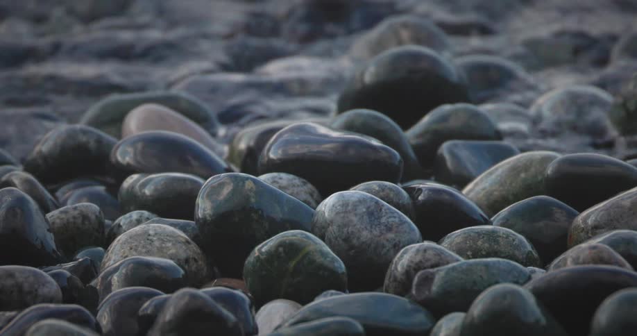 Close up on pile of black smooth rocks as the tide rolls over them