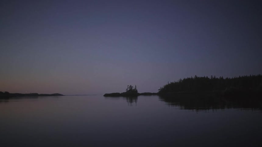 Ripples in the water disturb the reflection of the forested shore at night