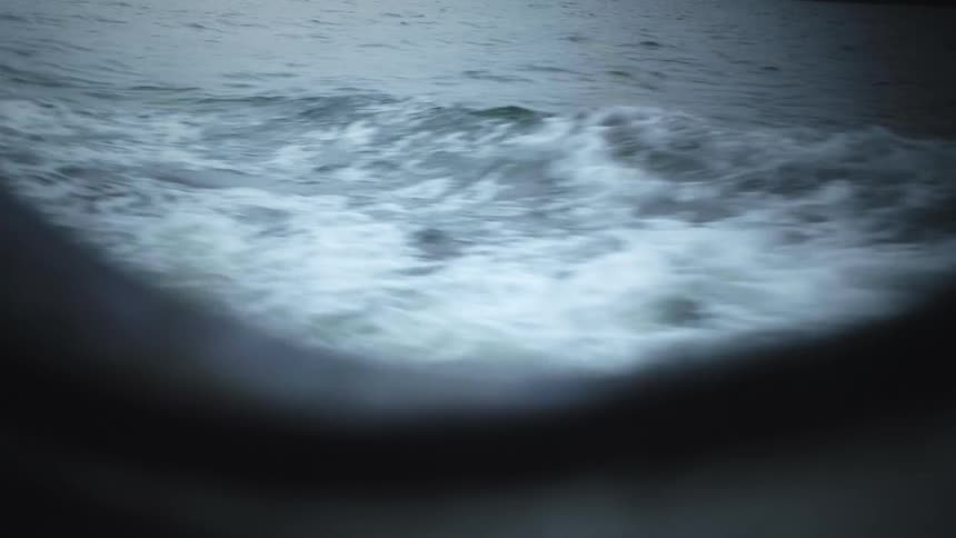 Looking out from a window inside a boat the shot captures the churning foamy wake as the vessel moves through the water