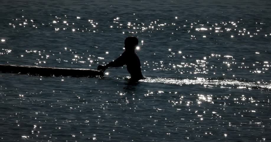 A boy grabs the floating wooden platform in the ocean
