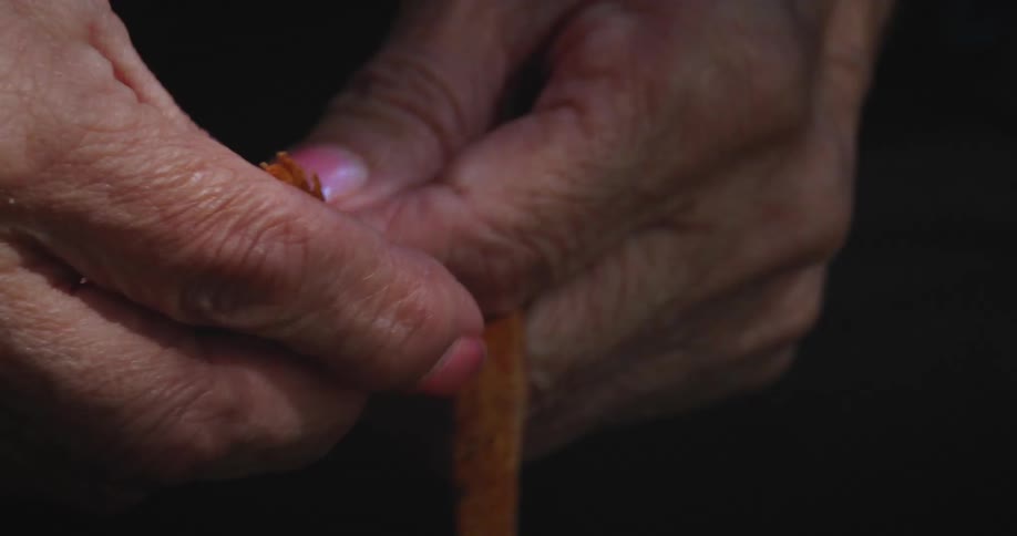 An overhead closeup shows hands carefully breaking apart pieces of a golden resinous substance possibly copal the subtle light illuminates the detailed texture of the material and the delicate movements of the fingers