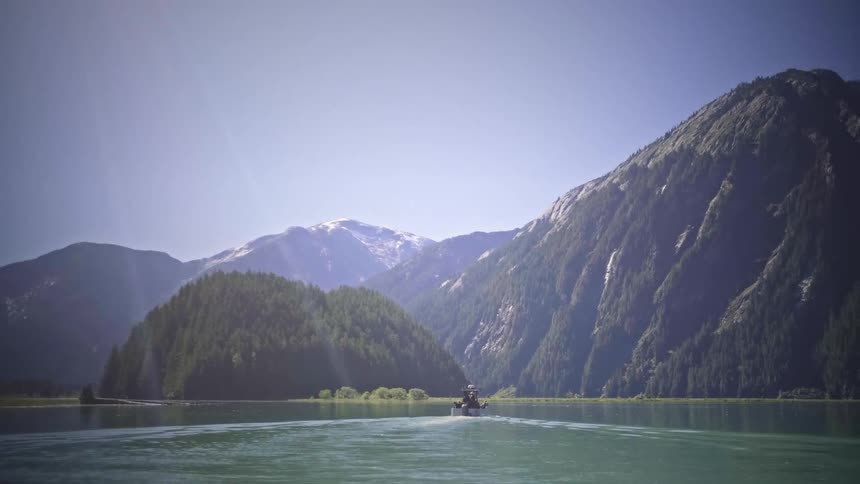 Person riding a motorboat on a calm lake surrounded by tall forested mountains