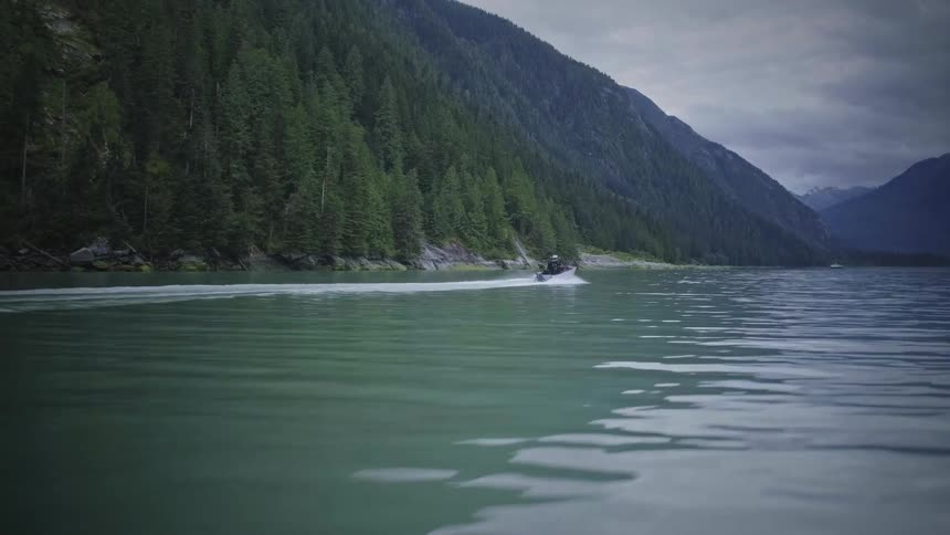 Boat moving through the sea surrounded by mountains with conifers