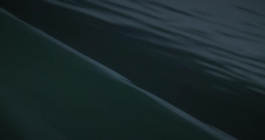 A closeup view from a moving boat shows its hull cutting through dark water creating ripples on the surface at night