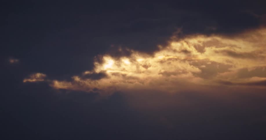 A break in dark clouds reveals glowing golden sunlight during a sunset