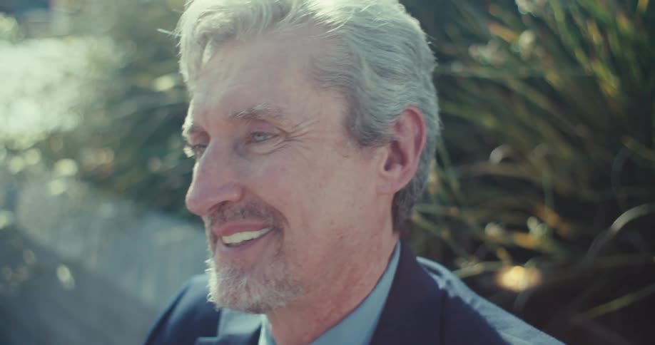 A man standing outdoor at daytime smiles after typing on his smartphone