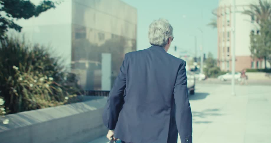 A joyful businessman walks briskly down a sunny city street with a briefcase