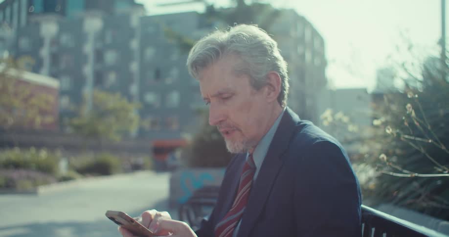 Man in suit sitting on a public bench interacting with a smartphone