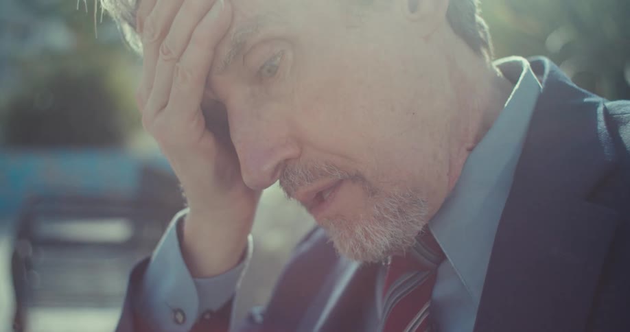 A closeup of an older man with a serious expression captures the sunlight softly illuminating his face and highlighting his blue eyes and graying beard