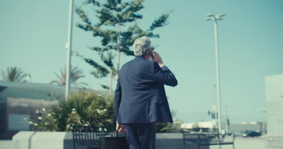A man wearing a suite and with a briefcase walking and talking on phone and smiling too