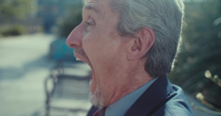 Businessman shouts and laughs excited by what he is reading on his smartphone while sitting on a bench outdoors in an urban environment