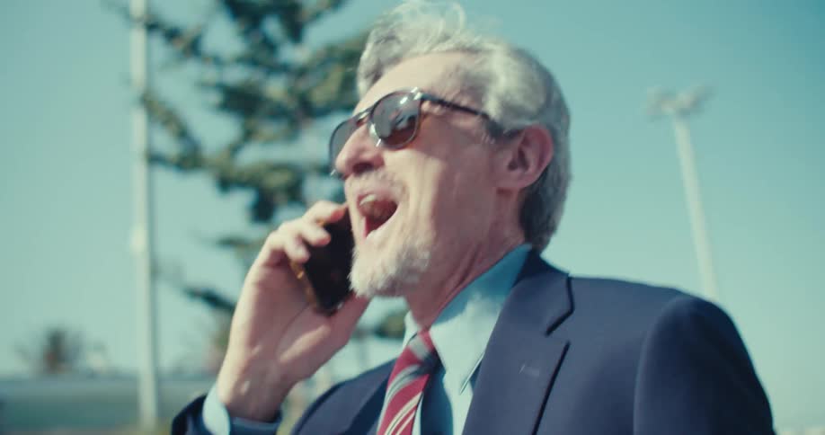 Older businessman walking in the city smiles while on a phone call then celebrates after hanging up