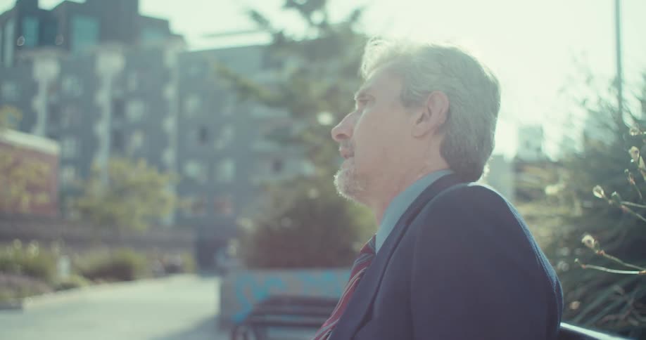 Man in suit sitting on public bench and interacting with smartphone with puzzled expression
