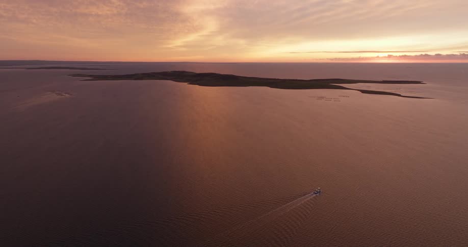 Panorama of a detached boat traveling on an ocean with an island in the background