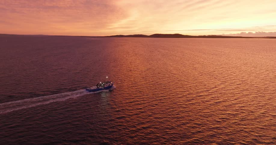 Boat sails across a calm sea under a vibrant orange sunset
