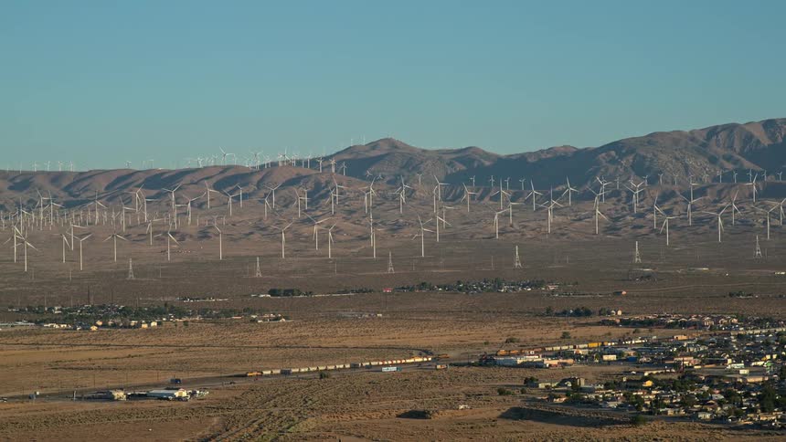 Aerial view of a city in a rural area with wind power stations in the mountains in the background