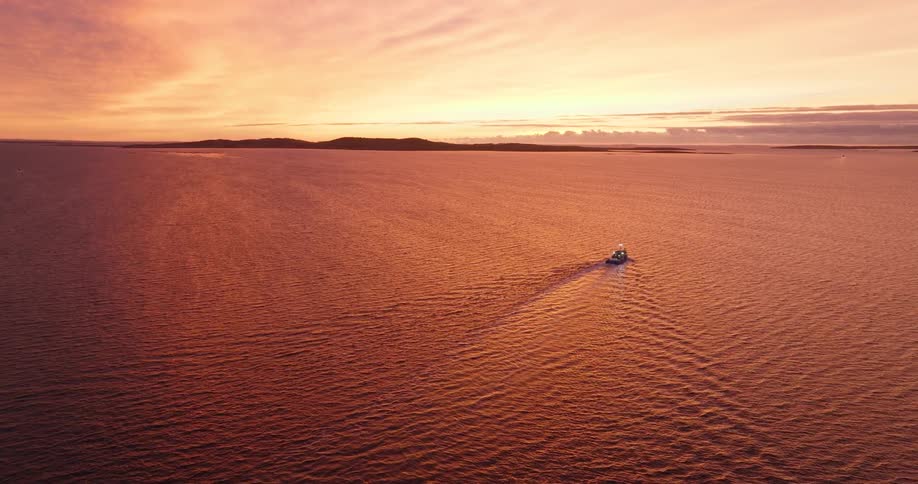 A boat sails across a calm ocean under a vivid orange sunset sky
