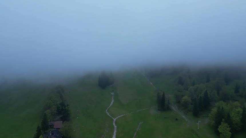 A foggy aerial view of a green valley with winding paths and scattered trees