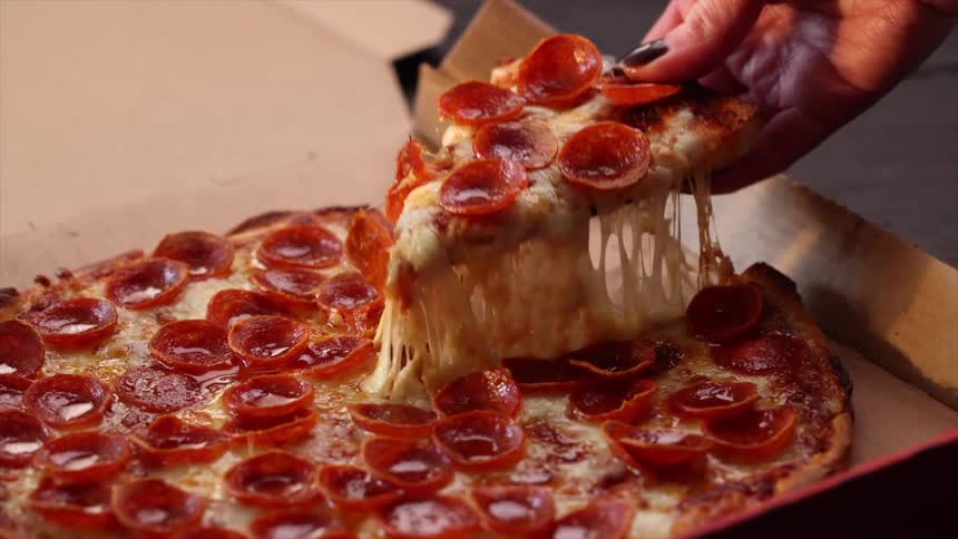 A hand lifts a slice of pepperoni pizza with long stretchy melted cheese trailing behind