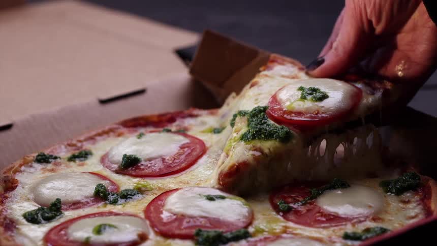 Woman picks up a slice of pizza from a delivery box resulting in long strands of cheese