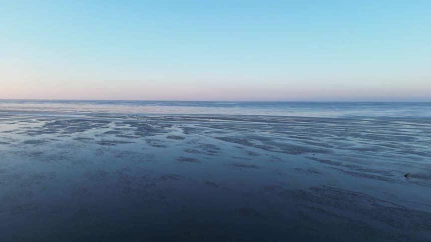 Serene coastal landscape at dusk with rippled sand and calm water