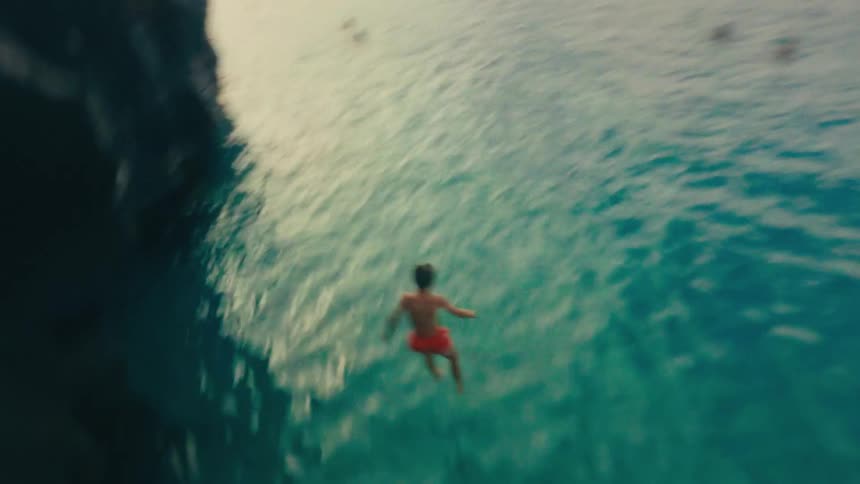 Boy in red swim shorts cliff jumping into the ocean