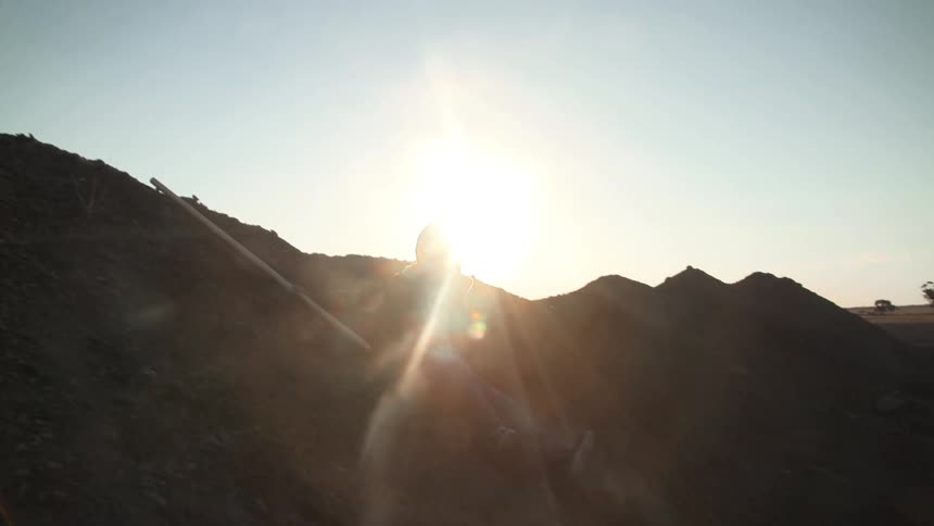 A person dressed in battle armor jumps from a hilltop