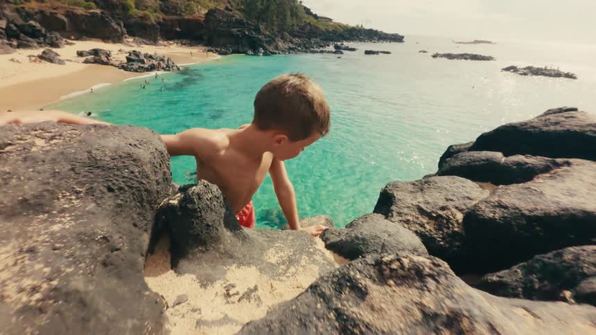 Little boy walking between rocks by the sea