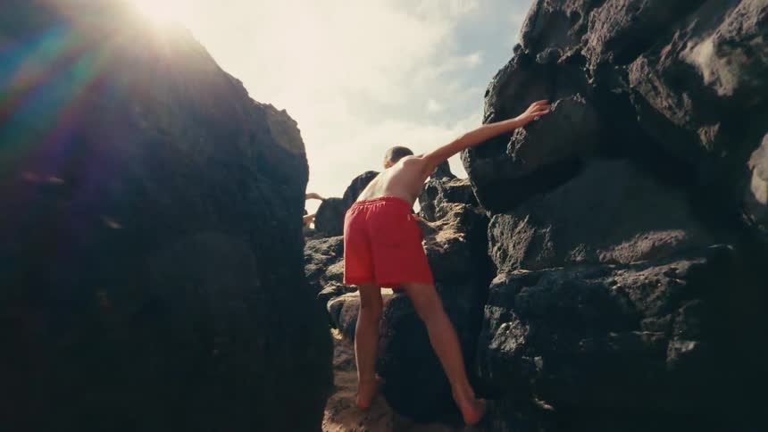 Family wearing swimwear climbs over the rocks on the coast on a cloudy summer day