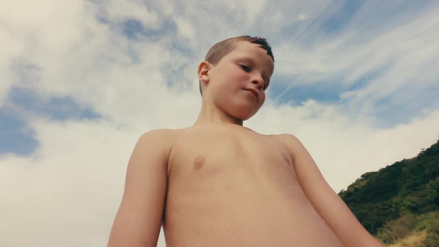 Boy stands outdoors near a hill with others on a cloudy day