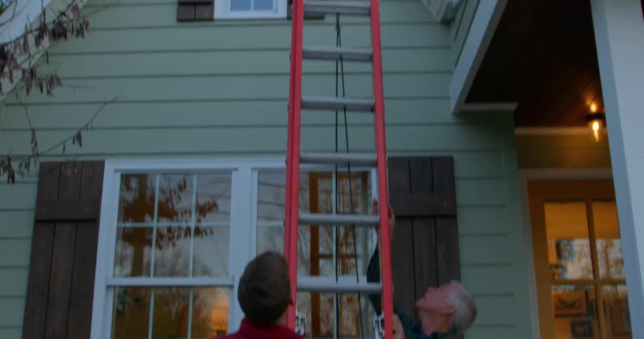 Father and son placing a long red ladder against front of house under the eaves
