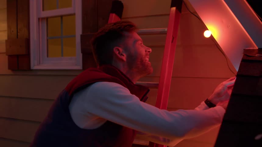Man outside a house installing christmas lights at night