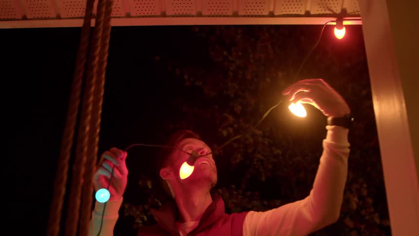 Man outside a house at night installing christmas lights