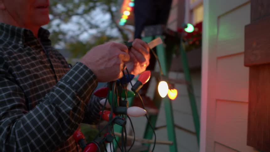 Man outside a house with another person holding lit christmas lights