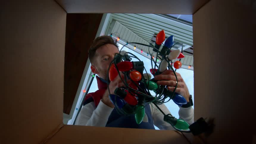 A partially obscured male face is seen through a tangle of dark cords and lights in a box
