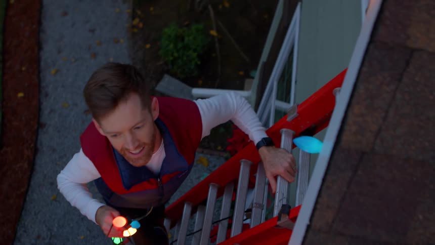 A man climbing a ladder to the roof while holding bright lights