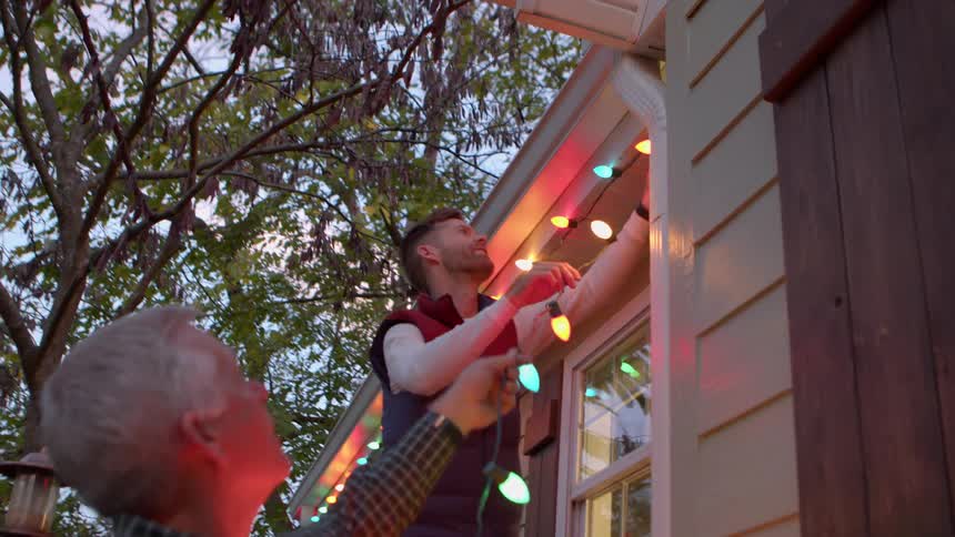 Two men installing christmas lights on the outside of a house