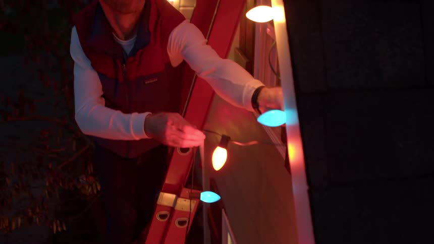 Man standing outside a house window and installing christmas lights at night