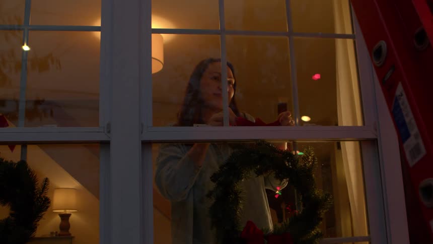 Woman installing a wreath on the window of the interior of the house