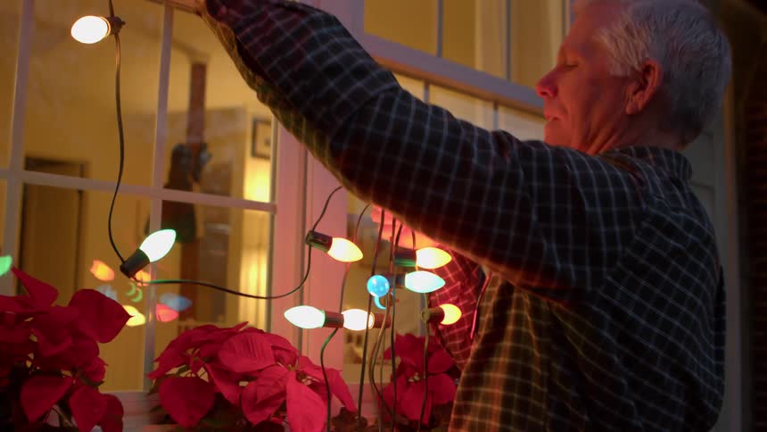 A man hangs string lights under the roof at dusk