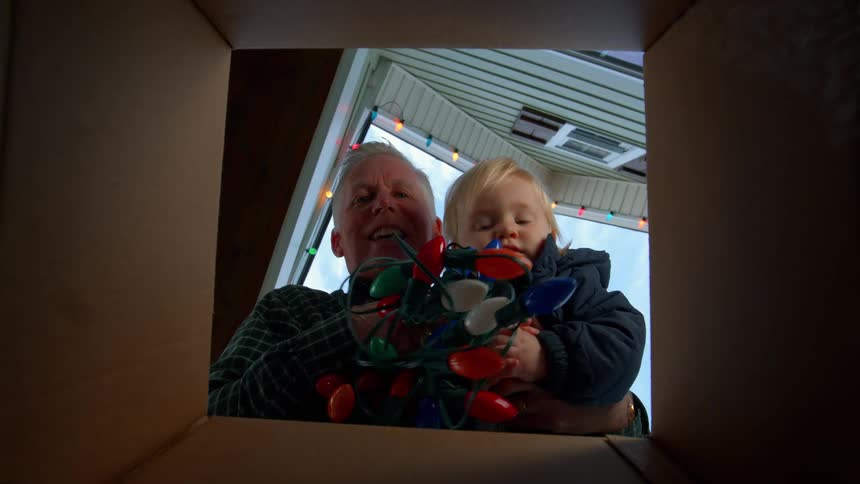 Man with a child on his lap taking christmas lights from a box