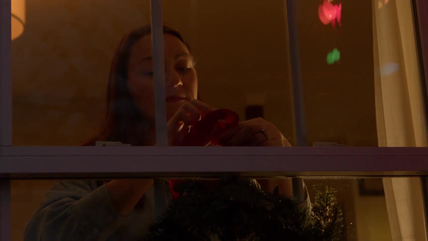 Woman tying a christmas wreath on the window