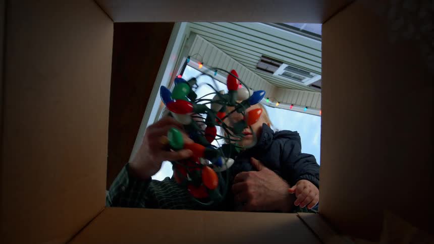 Man with a child on his lap picking up christmas lights from a box