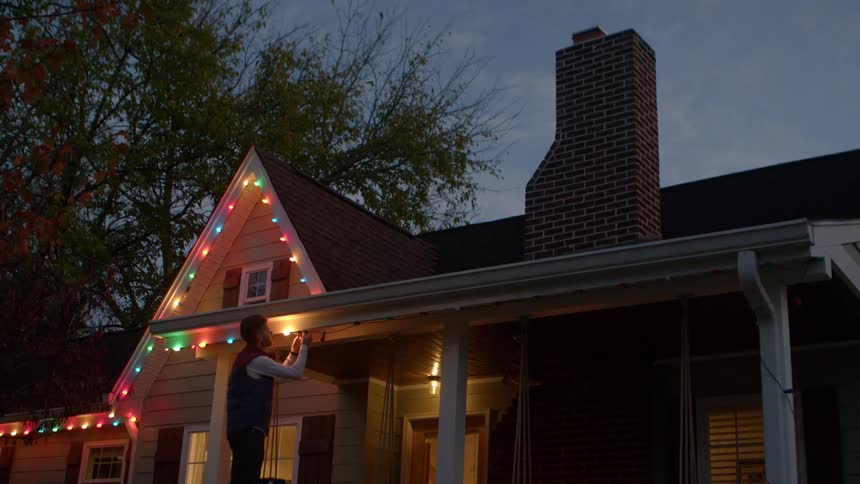 A man is hanging christmas lights on the ladder