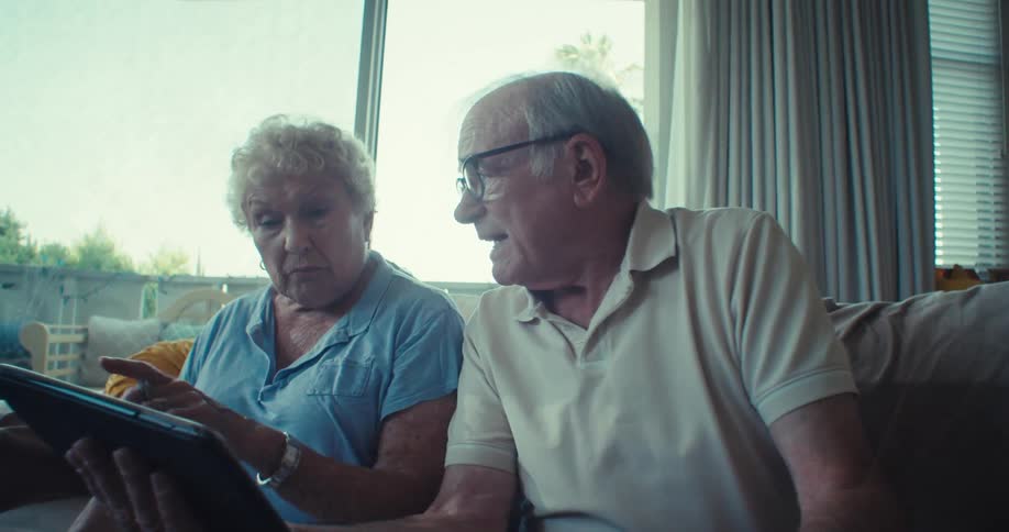 Elderly man next to an elderly woman both sitting watching on a tablet
